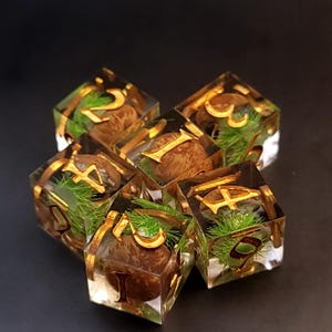 May include: Set of six clear resin dice with gold numbers and green moss inside. Each die has a different number from 1 to 6.