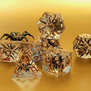 Könnte beinhalten: Ein Satz von sechs transparenten Würfeln mit goldenen Akzenten und einer Spinne, die in jedem Würfel eingeschlossen ist. Die Würfel befinden sich auf einer goldenen Oberfläche.