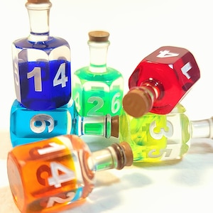 May include: Six colorful glass bottles with cork stoppers and numbered sides. The bottles are shaped like dice and are filled with colored liquid. The bottles are arranged in a pile on a white surface.