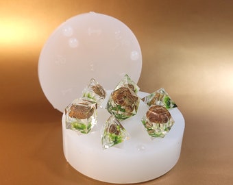 May include: Six clear resin dice with brown and green botanical inclusions inside. The dice are sitting on a white silicone mold.