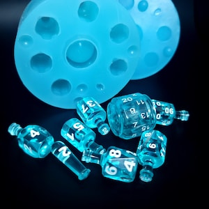 May include: A set of blue dice with white numbers, including a d20, d10, d8, d6, and d4. The dice are sitting on a blue silicone mold with multiple circular indentations.