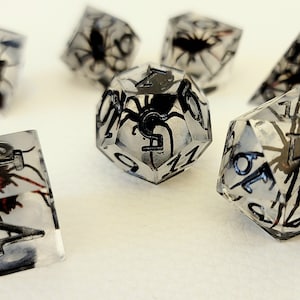 May include: A set of clear dice with black spider and number details. The dice are in various shapes, including a d4, d6, d8, d10, d12, and d20.