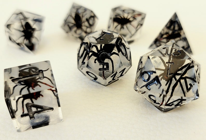 May include: A set of clear dice with black spider and number details. The dice are in various shapes, including a d4, d6, d8, d10, d12, and d20.