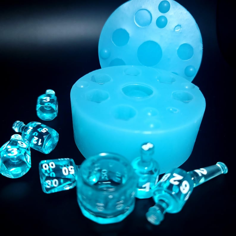 May include: A blue silicone mold for making dice, with a lid and several clear blue dice with white numbers on them.