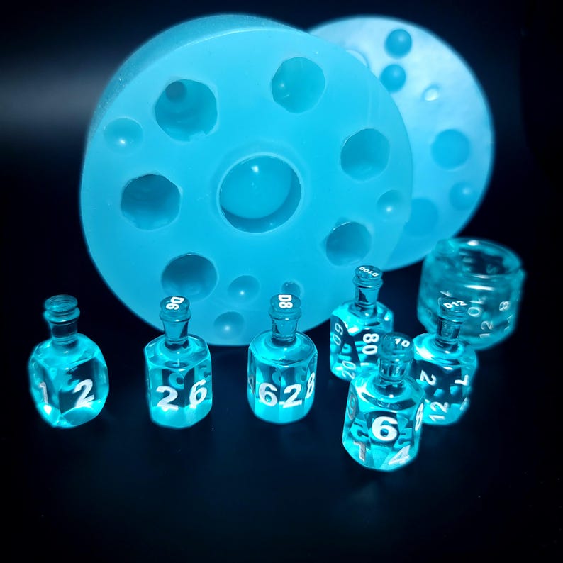 May include: A set of blue glass dice with white numbers, including a D6, D8, and a few other dice. The dice are sitting on a black surface next to a blue silicone mold.