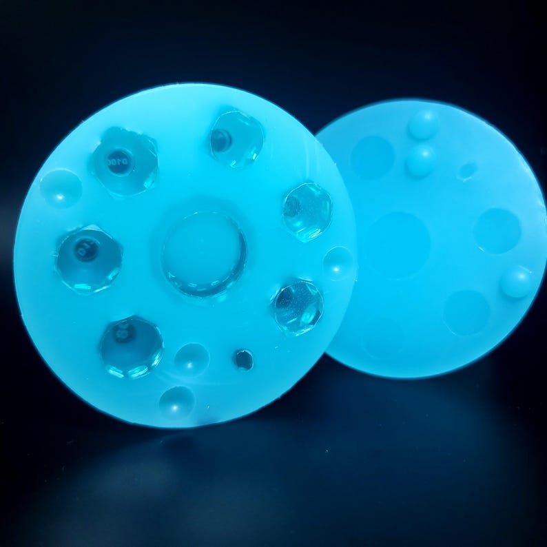 May include: Two light blue silicone molds with circular shapes. One mold has a large circle in the center and several smaller circles around it. The other mold has several smaller circles.