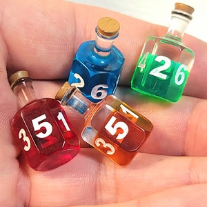 May include: Four small glass bottles with cork tops, each filled with a different coloured liquid and numbered with white numbers. The bottles are shaped like dice and are used for playing games.