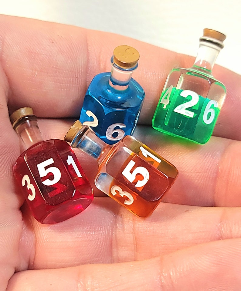 May include: Four small glass bottles with cork tops, each filled with a different coloured liquid and numbered with white numbers. The bottles are shaped like dice and are used for playing games.