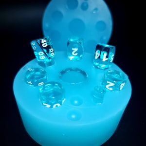 May include: A blue silicone mold with seven clear dice inside. The dice have white numbers on them.