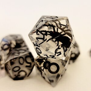 May include: A set of six clear resin dice with black numbers and a spider encased in each die.