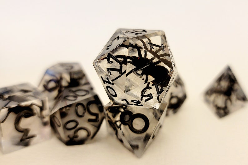 May include: A set of six clear resin dice with black numbers and a spider encased in each die.