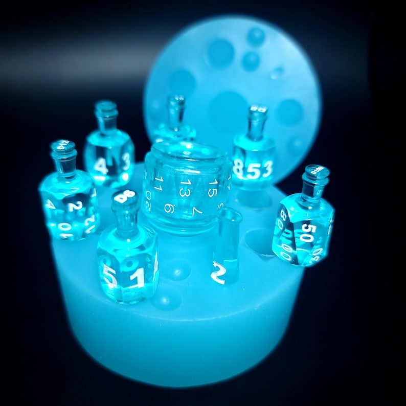 May include: A blue silicone mold for making dice. The mold has seven circular depressions, each with a different number of sides. There are six blue dice in the mold, each with white numbers.