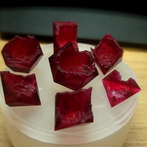 May include: A collection of seven deep red, faceted, gemstone-like dice in a white plastic container.