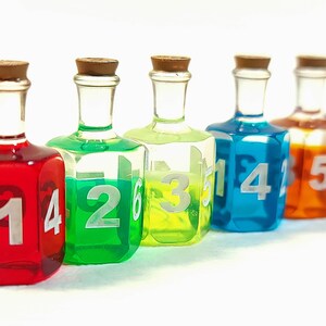 May include: Six small glass bottles with cork tops, each filled with a different coloured liquid. The bottles are numbered 1 through 6, with the numbers visible on the front of each bottle.