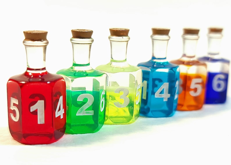 May include: Six small glass bottles with cork tops, each filled with a different coloured liquid. The bottles are numbered 1 through 6, with the numbers visible on the front of each bottle.