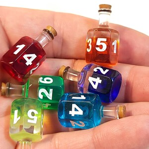 May include: Six colourful glass dreidels with numbers 1, 2, 3, 4, 5, and 6. The dreidels are in a hand, and each dreidel has a cork top.