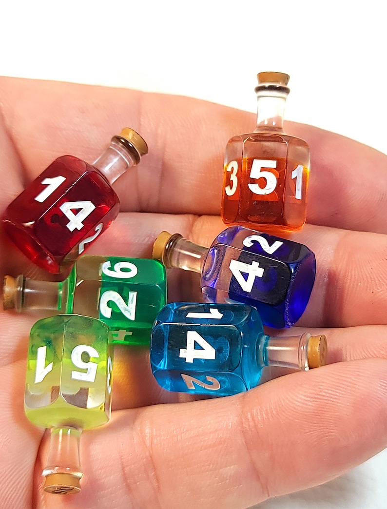 May include: Six colourful glass dreidels with numbers 1, 2, 3, 4, 5, and 6. The dreidels are in a hand, and each dreidel has a cork top.