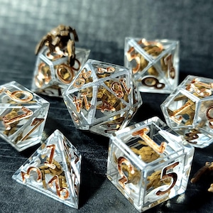 May include: A set of seven polyhedral dice made of clear resin, each containing a small, brown, textured creature figure inside. The numbers on the dice are embossed in a metallic copper color, with sharp edges and clear, transparent surfaces.