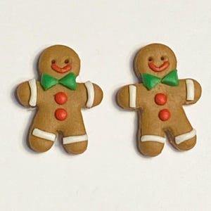 May include: Two gingerbread man-shaped Christmas ornaments with white icing, green bow ties, and red buttons.
