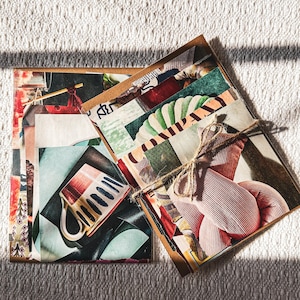 May include: A stack of vintage postcards with colorful images and patterns, tied together with twine. The postcards feature a variety of subjects, including a cup, a fruit, and a person.