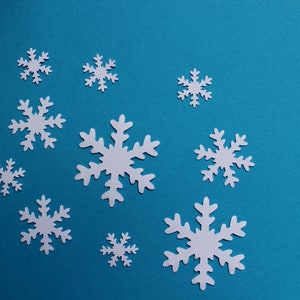 Könnte beinhalten: Ein blauer Hintergrund mit weißen Papierschneeflocken in verschiedenen Größen.