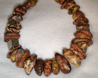 May include: A brown, yellow, and black stone necklace with a silver clasp and a silver charm with a geometric design.