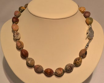 May include: A necklace made of brown, pink, and white patterned oval beads with a silver snake clasp.