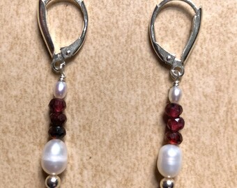 May include: A pair of silver dangle earrings with a white pearl and red gemstones.