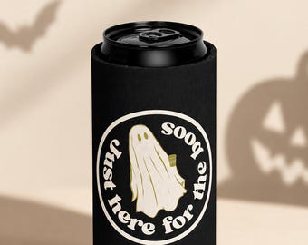 Puede incluir: Un enfriador de latas de espuma negra con un gráfico circular que muestra una ilustración de un fantasma blanco y el texto Just here for the boos en una fuente curva. El enfriador es cilíndrico y rodea una lata de metal.