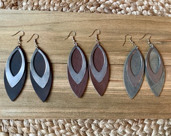 May include: Three pairs of layered leather earrings. Each pair features two overlapping oval-shaped leather pieces in different shades of brown and grey. The earrings have silver-toned hooks.