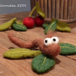 May include: A brown felt worm with white eyes and green felt leaves. The text "Süβes Würmchen EDDI" is visible in the background.