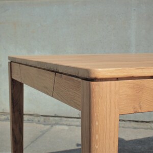 May include: A light brown wooden table with a rectangular top and four square legs. The table has a natural wood grain finish and appears to be made of solid wood. The table's dimensions are not visible in the image.