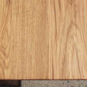 May include: Close-up of a light brown wooden table surface. The wood grain is visible, with a natural pattern and texture. The corner of the table is rounded. The wood has a warm, inviting tone.