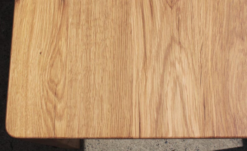 May include: Close-up of a light brown wooden table surface. The wood grain is visible, with a natural pattern and texture. The corner of the table is rounded. The wood has a warm, inviting tone.