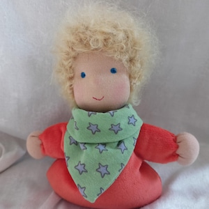 May include: A handmade doll with blonde curly hair, wearing a red shirt and a green bandana with white stars.
