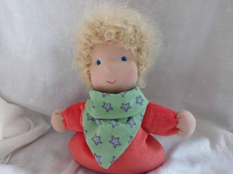 May include: A handmade doll with blonde curly hair, wearing a red shirt and a green bandana with white stars.