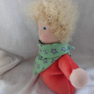 May include: A handmade doll with blonde curly hair, wearing a green and blue star patterned scarf and a red shirt.