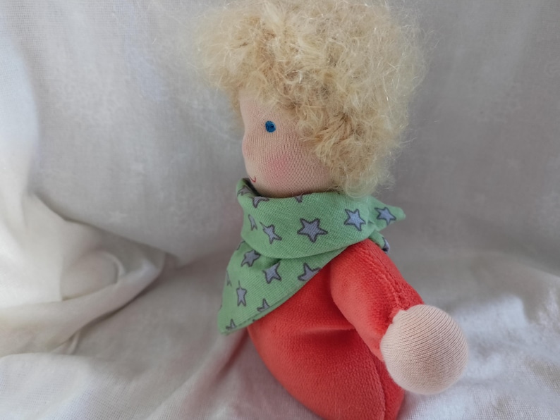 May include: A handmade doll with blonde curly hair, wearing a green and blue star patterned scarf and a red shirt.