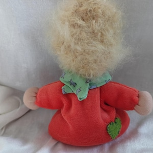 May include: A handmade doll with blonde curly hair, wearing a red dress with a green and white star patterned scarf and a green heart patch.