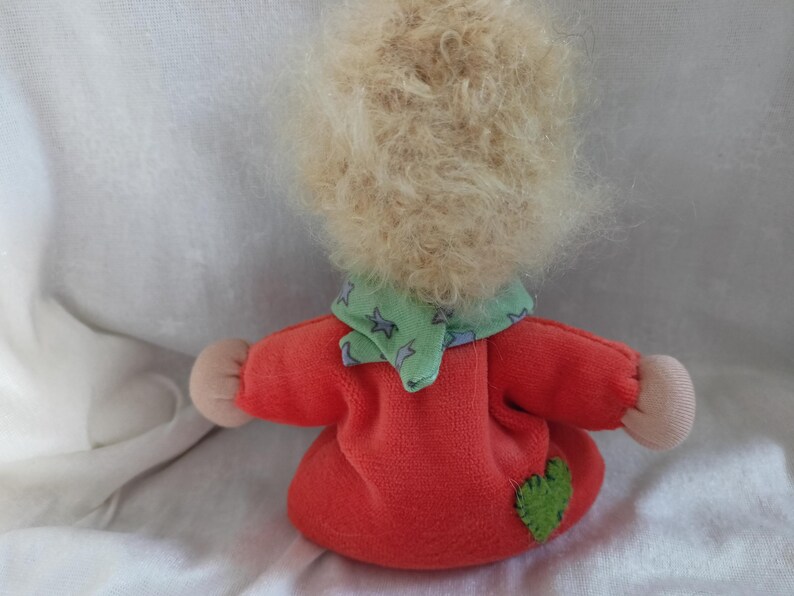 May include: A handmade doll with blonde curly hair, wearing a red dress with a green and white star patterned scarf and a green heart patch.