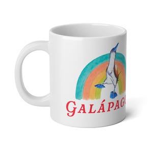 May include: White ceramic mug featuring a watercolor illustration of a blue-footed booby bird, a rainbow, and the word "Galápagos" in red. The mug has a curved handle and is suitable for hot or cold beverages.