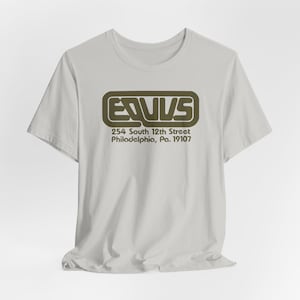 May include: A light gray short-sleeve t-shirt featuring a dark olive green graphic on the chest. The graphic displays the text "EQUUS" inside a rounded rectangular border, followed by the address "254 South 12th Street Philadelphia, Pa. 19107".