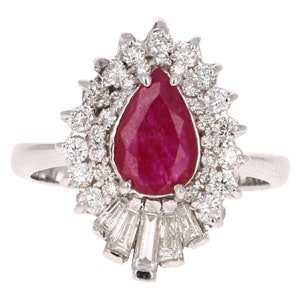 Puede incluir: Un anillo de rubí en forma de pera engastado en oro blanco con un halo de diamantes redondos brillantes y una fila de diamantes baguette.