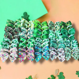 May include: A collection of 40 green shamrock patterned hair bows. The bows are arranged in rows, with each row featuring a different shamrock design. The bows are made of green and white ribbon and are perfect for adding a touch of Irish charm to any outfit.