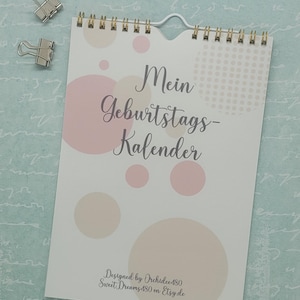 Puede incluir: Un calendario blanco con una encuadernación en espiral dorada. La portada presenta un patrón de lunares rosa y beige con el texto "Mein Geburtstagskalender" en una fuente cursiva. La parte inferior de la portada tiene el texto "Designed by Orchidee480 SweetDreams480 on Etsy.de".