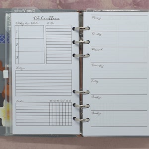 Op de afbeelding: Een witte planner met een zwart-wit raster op de rechterpagina. De linkerpagina heeft een sectie voor "Dagelijkse doelen" en "Te doen" met elk drie regels. Daaronder is een sectie voor "Notities" met acht regels en een sectie voor "Taken" met een raster.