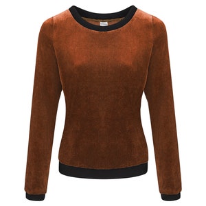 Könnte beinhalten: Ein langärmliges, braunes Samt-Sweatshirt mit schwarzem Besatz an Ausschnitt, Bündchen und Saum. Das Oberteil hat einen Rundhalsausschnitt und ein weiches, strukturiertes Aussehen. Das Kleidungsstück ist auf Komfort und Wärme ausgelegt.