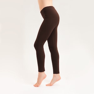 Könnte beinhalten: Eine braune Leggings an den Beinen einer Person. Die Leggings ist eng anliegend und hat eine glatte Textur.