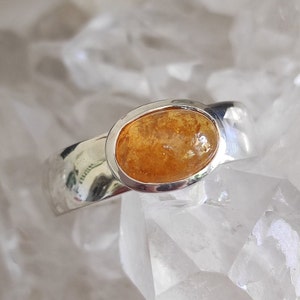 Può includere: Un anello d'argento con una pietra preziosa ambra di forma ovale incastonata in una montatura a castone.