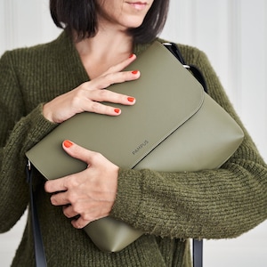 Pode incluir: Bolsa verde-oliva com fecho de aba, segurada por uma pessoa vestindo um suéter verde. A bolsa tem uma alça preta e a palavra "PAMPUS" é impressa na frente.
